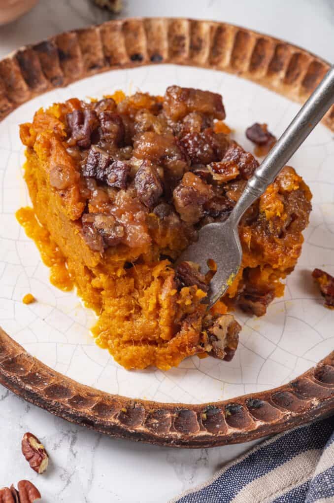 A fork getting a bite of sweet potato casserole from a serving on a small plate.