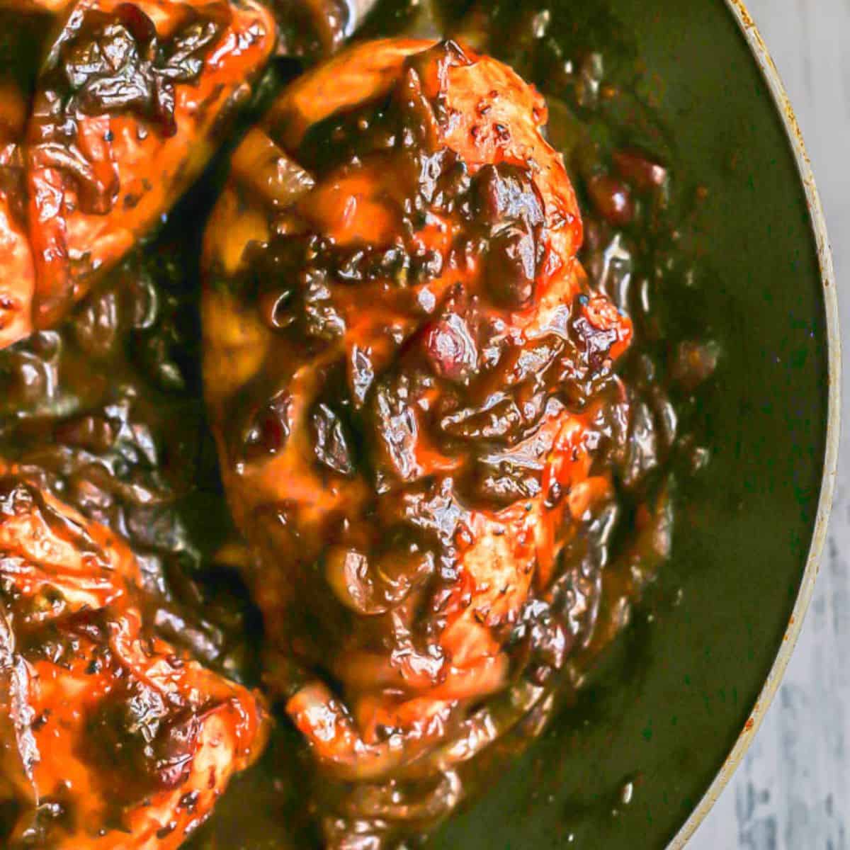 Close up of a seared chicken breast in a dark skillet with a cranberry balsamic sauce.