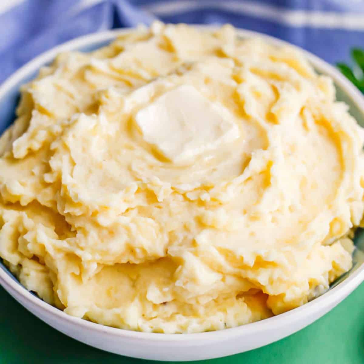 Close up of a blue and white bowl with fluffy homemade mashed potatoes with a pat of melting butter on top.