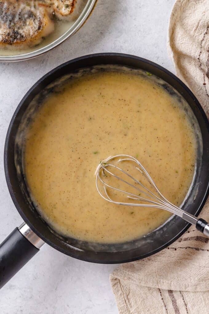 A smooth gravy in a large skillet with a whisk resting in it.