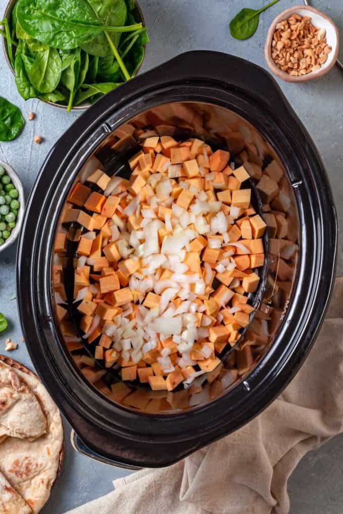 Diced onion and sweet potatoes in a slow cooker insert.