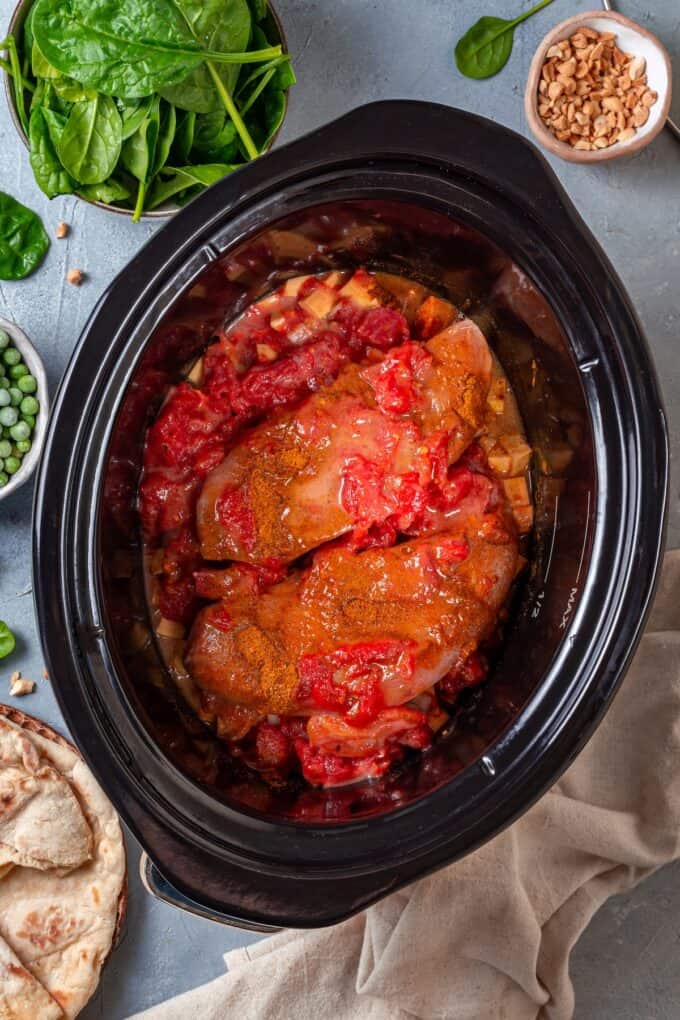 Seasoned chicken breasts topped with diced tomatoes in a slow cooker before being cooked.