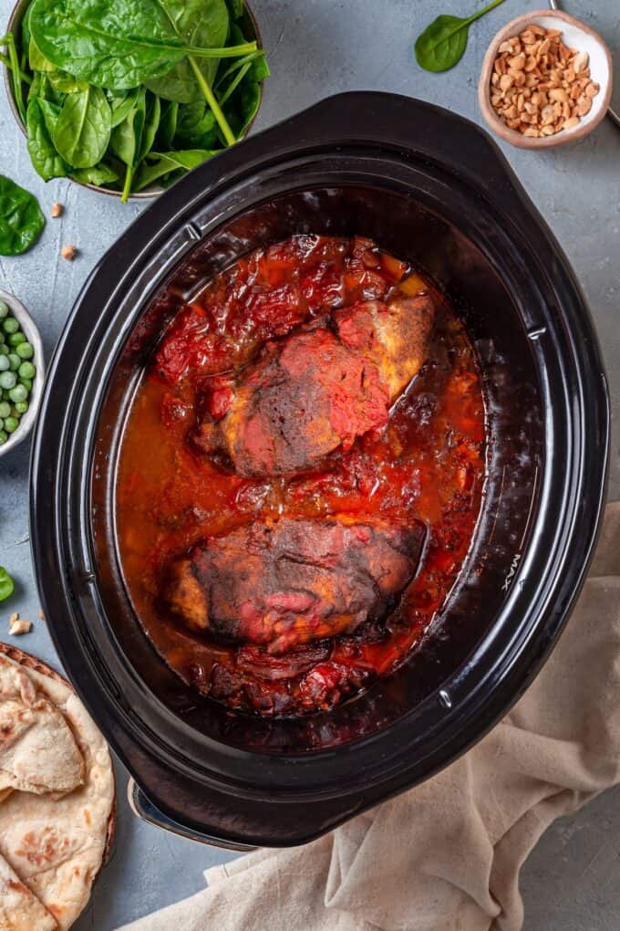 Cooked chicken breasts with diced tomatoes in a slow cooker insert.