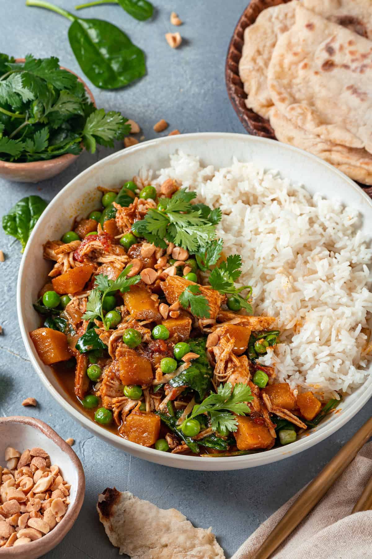 A bowl of steamed white rice alongside a chicken curry mixture with sweet potatoes, peas and spinach with naan bread to the side.