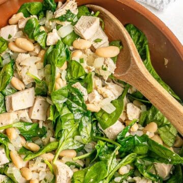 Close up of a wooden spoon resting in a copper skillet with a mixture of leftover turkey, white beans and wilted spinach.
