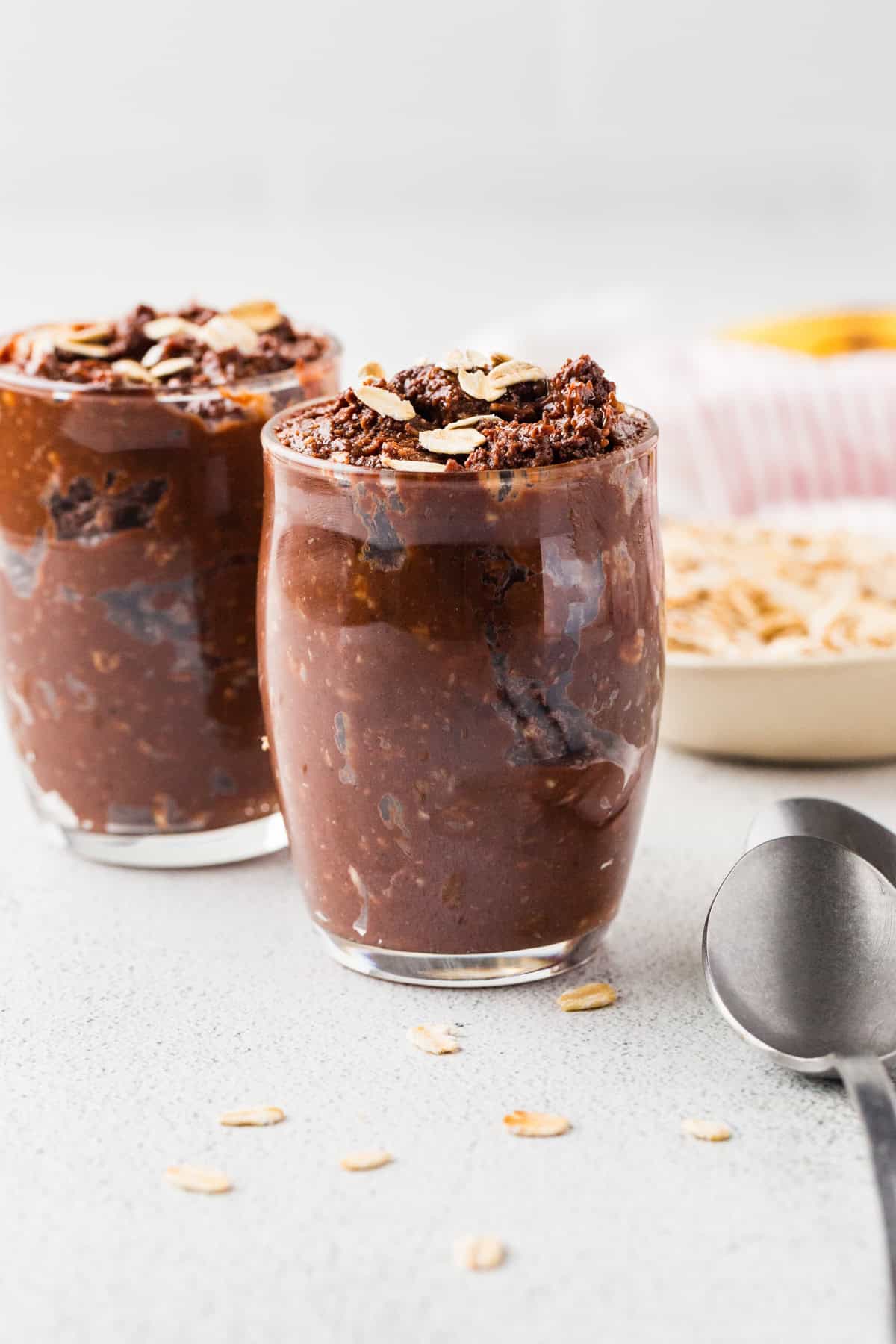 Two glass jars with a homemade healthy chocolate pudding dessert piled in and oats sprinkled on top.