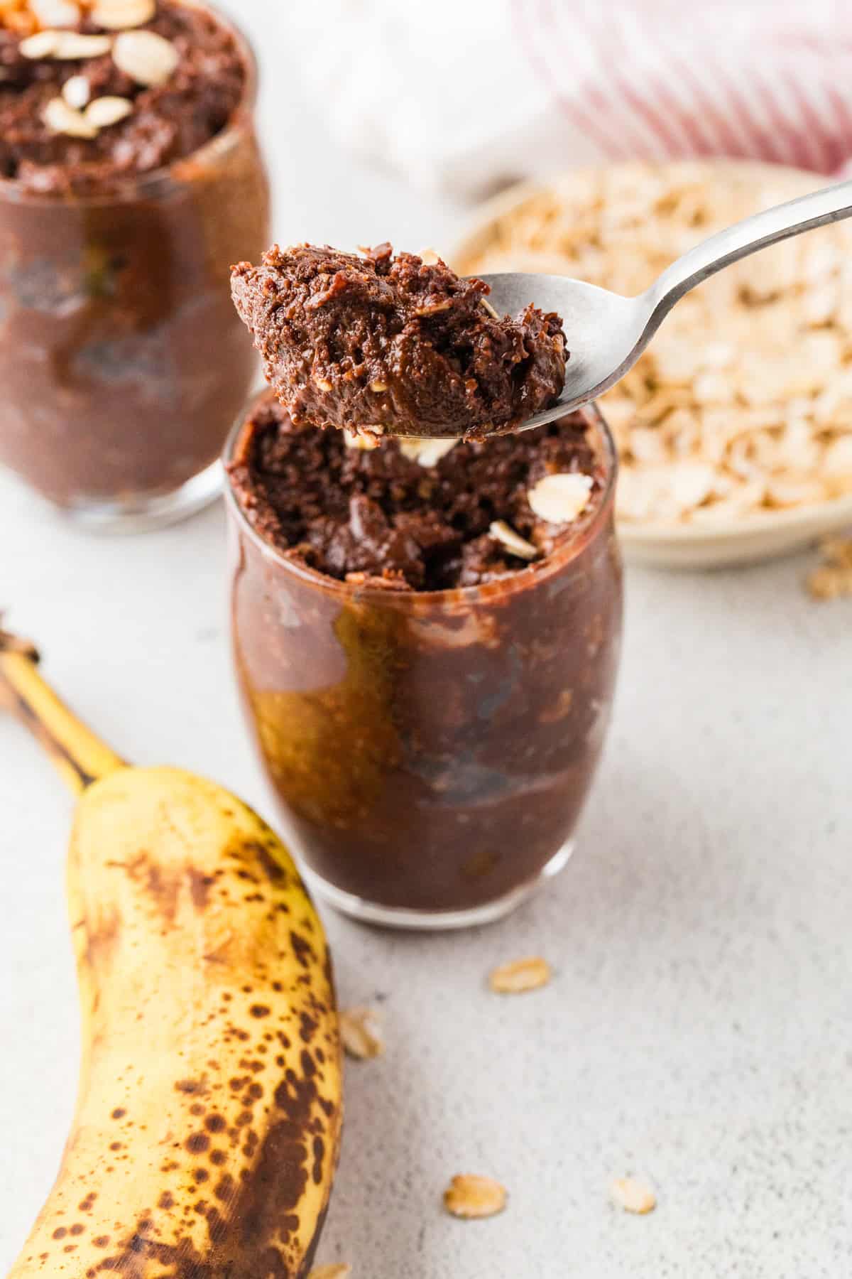 A spoon holding up a scoop of a healthy chocolate pudding mixture from a glass jar.