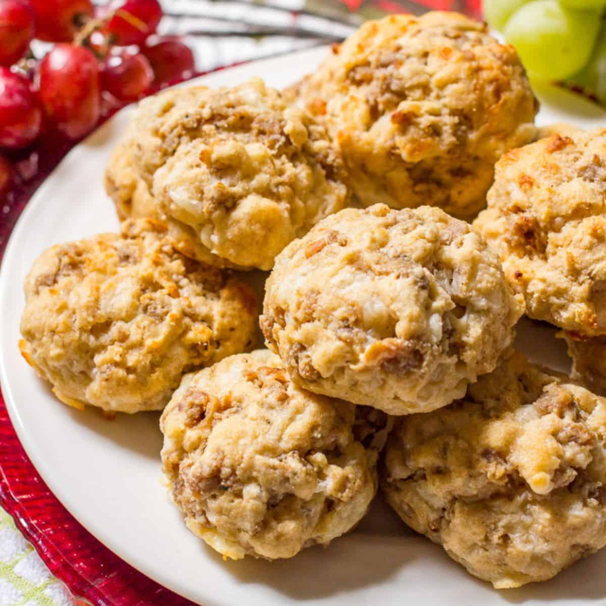 Close up of a plate full of stacked homemade sausage biscuit balls with some red and green grapes in the background.