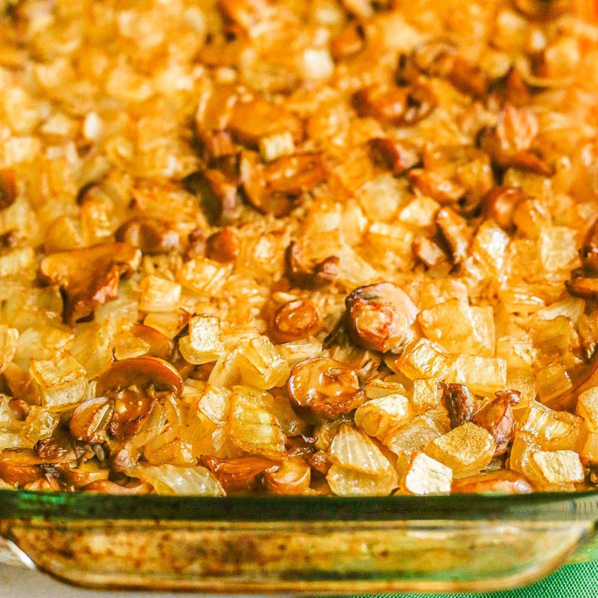 Close up of a baked mushroom rice casserole with onions and beef broth in a clear glass baking dish.