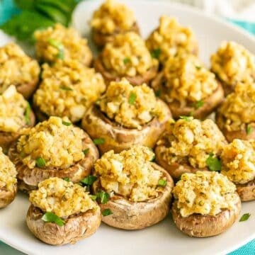 Close up of stuffed mushrooms on a round white plate with fresh herbs sprinkled on top.