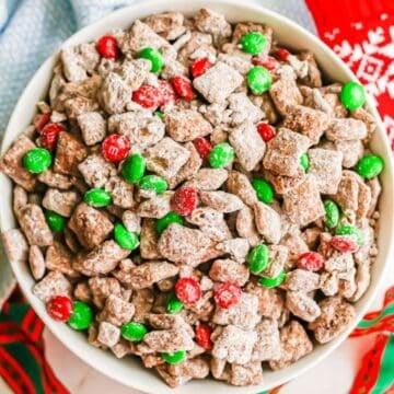 Close up of a white bowl filled with reindeer chow snack mix with red and green M&Ms mixed in.