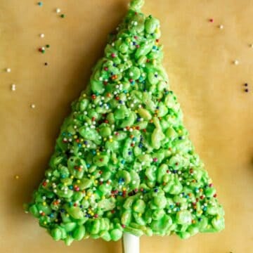 Close up of a rice krispie treat dyed green and shaped like a Christmas tree with sprinkles on it for decoration.