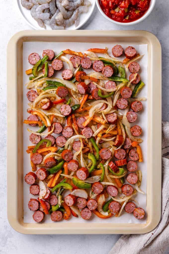 Sliced andouille sausage and onions and peppers on a sheet pan before being roasted.