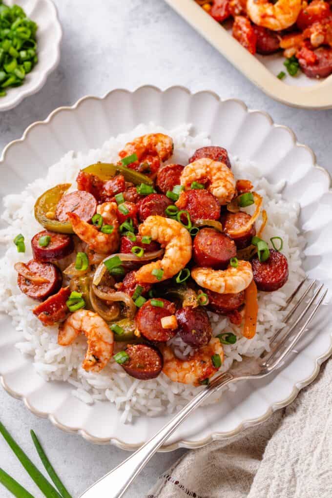 Jambalaya with andouille and sausage served over steamed white rice on a plate with a fork to the side.