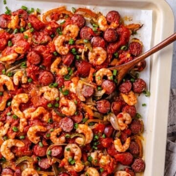 Close up of a wooden spoon scooping up some shrimp and andouille from a sheet pan jambalaya.