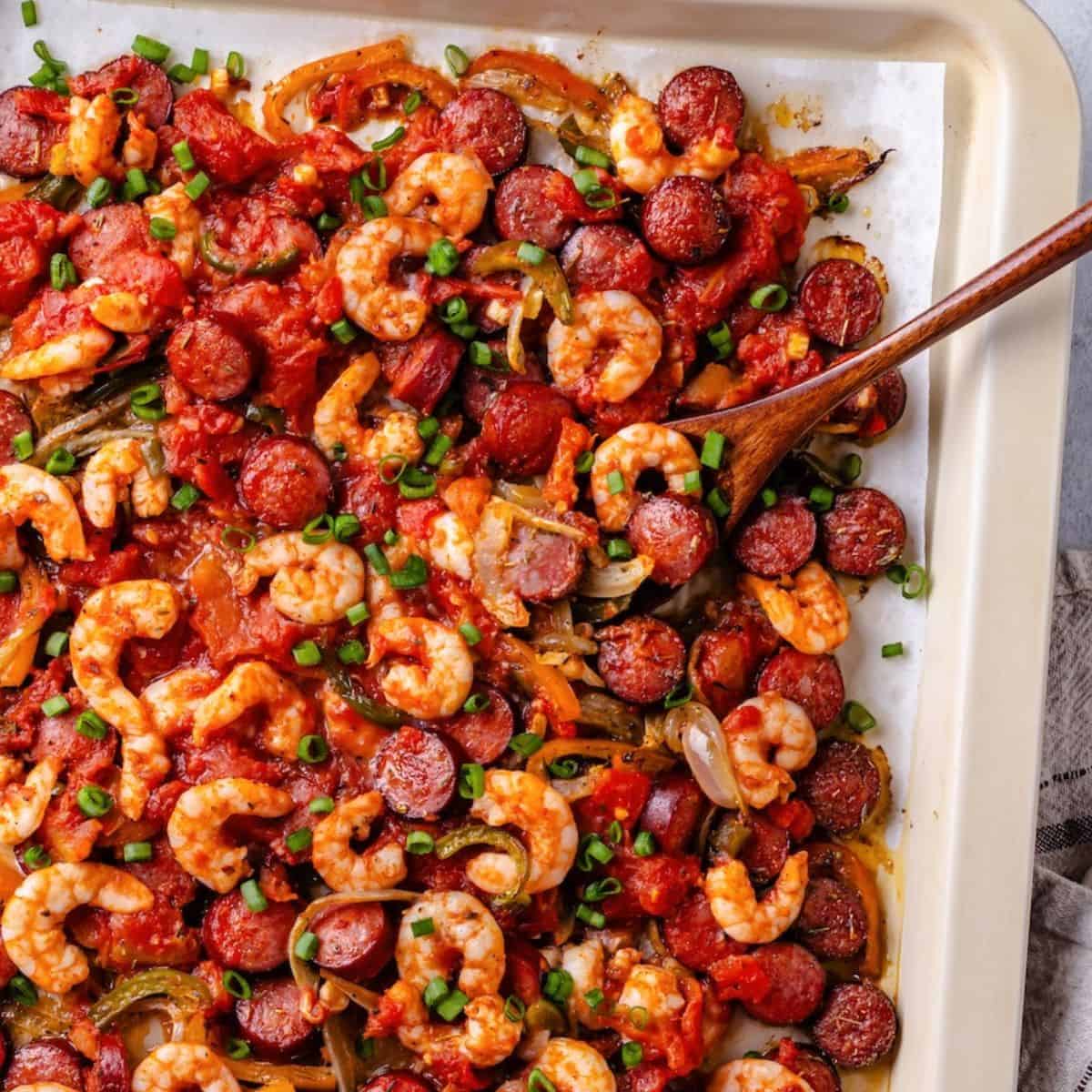 Close up of a wooden spoon scooping up some shrimp and andouille from a sheet pan jambalaya.