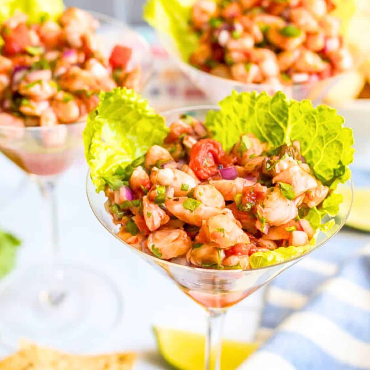 Close up of martini glasses lined with lettuce leaves and filled with a shrimp salsa mixture as an appetizer.
