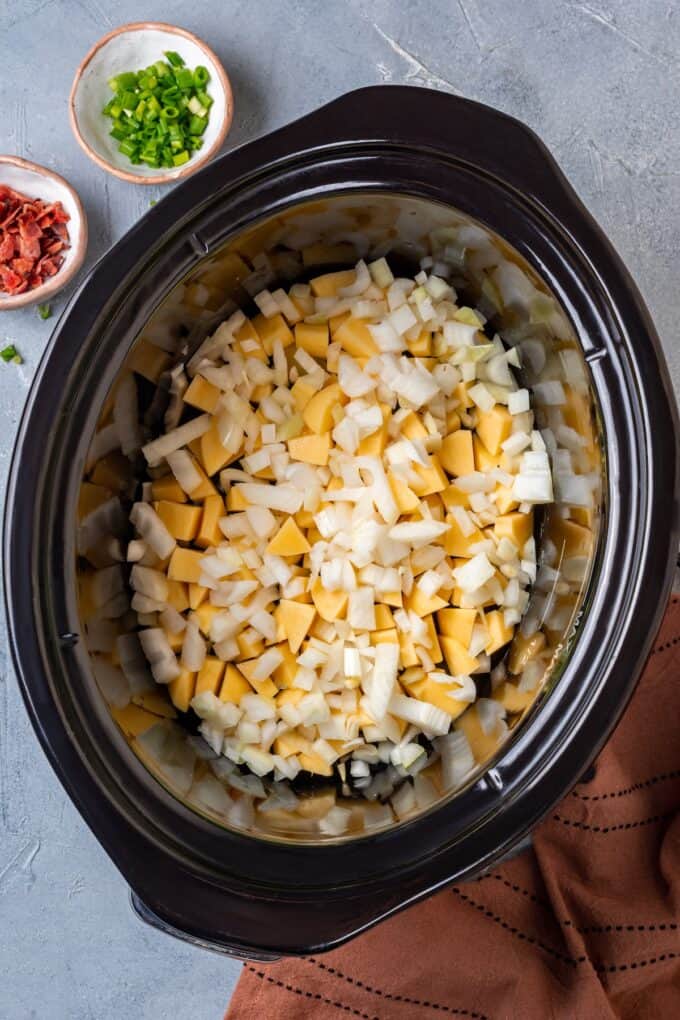 Chopped onion and potatoes in a slow cooker insert.