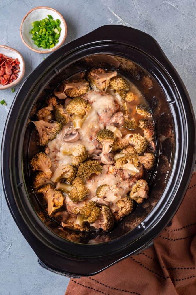 A black slow cooker with cooked chicken, broccoli and potatoes.