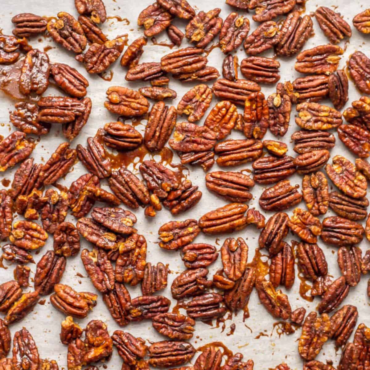 Close up of a parchment paper lined sheet pan filled with roasted sweet and spicy pecans with a maple syrup glaze.