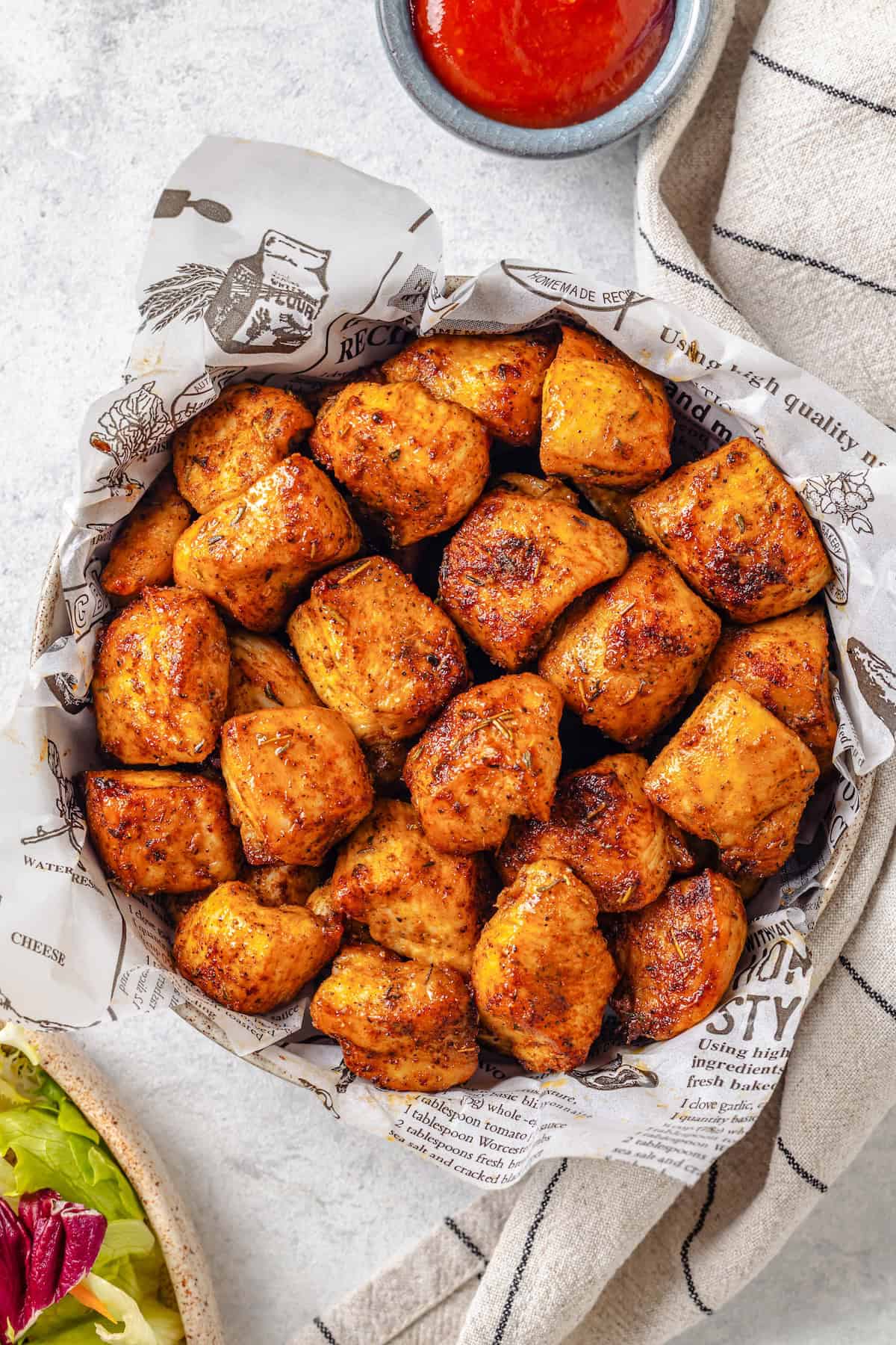 Seasoned, cooked Air Fryer chicken bites in a bowl with a bowl of ketchup for dipping nearby.