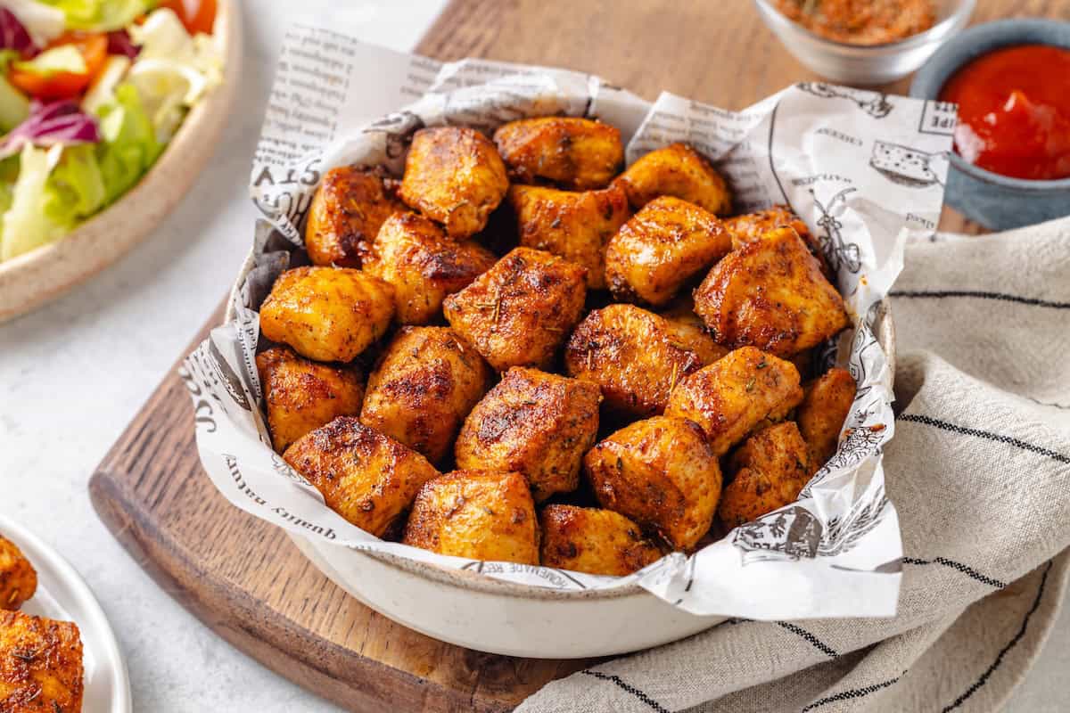Air Fryer chicken bites served in a bowl with ketchup to the side and a salad bowl in the background.