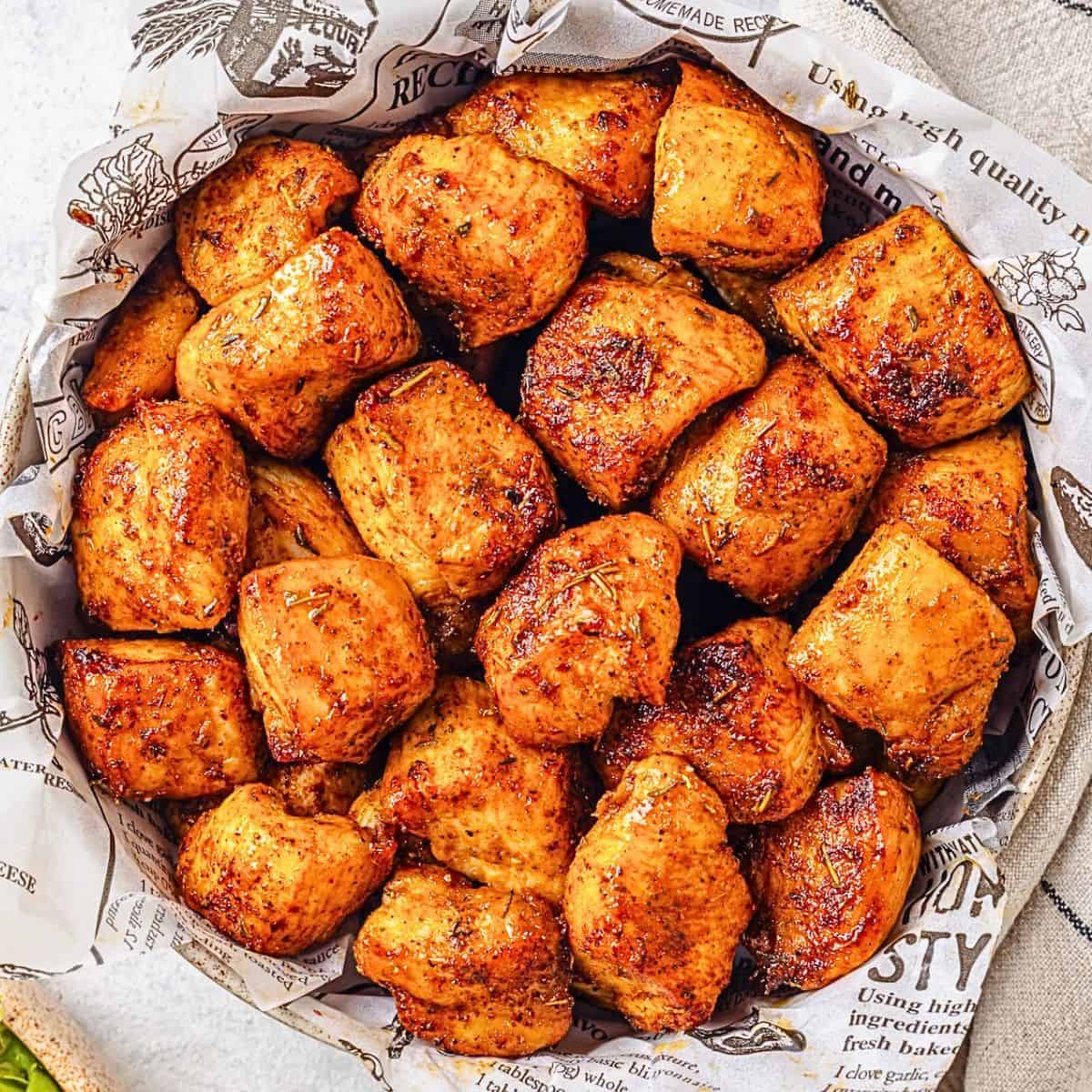 Close up of seasoned, cooked Air Fryer chicken bites in a bowl with a bowl of ketchup for dipping nearby.