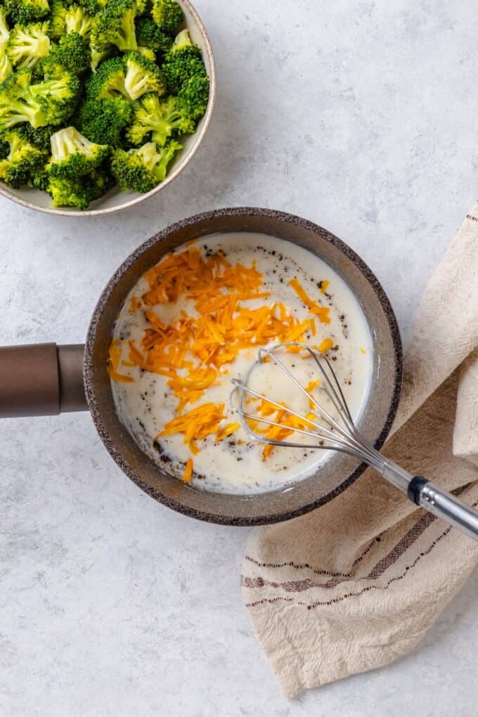 Shredded cheddar cheese being stirred into a small pot for making a cheese sauce.