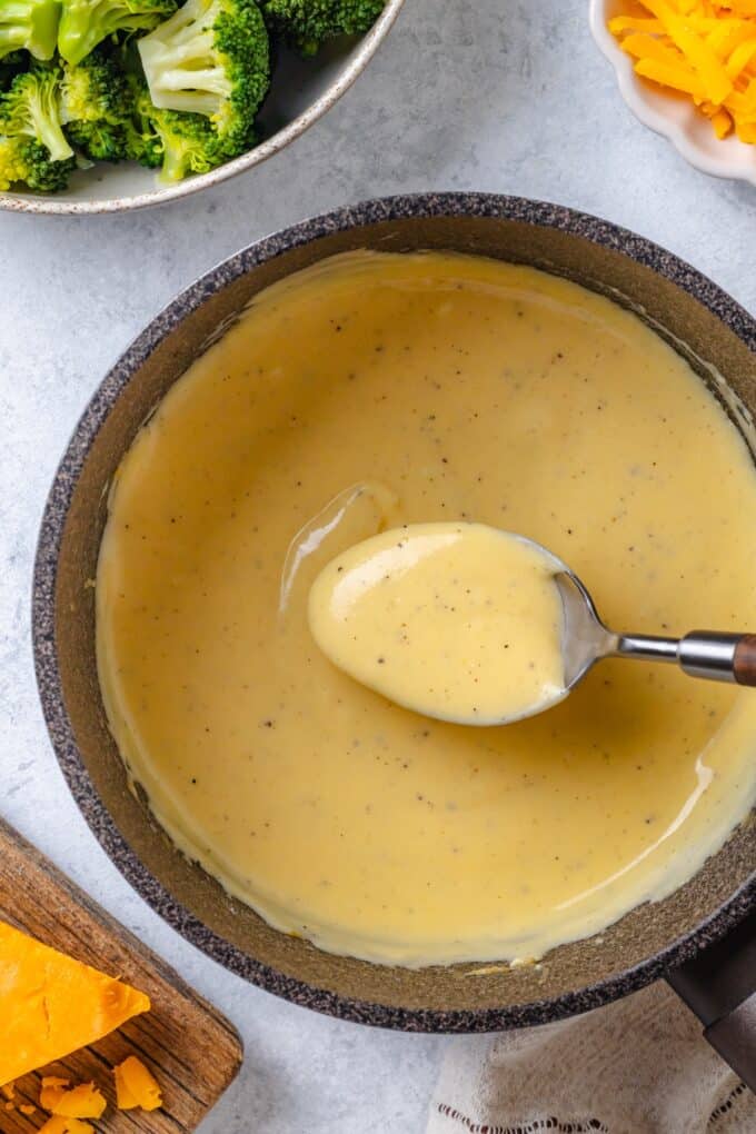 A spoon holding up a cheese sauce from a small saucepan.