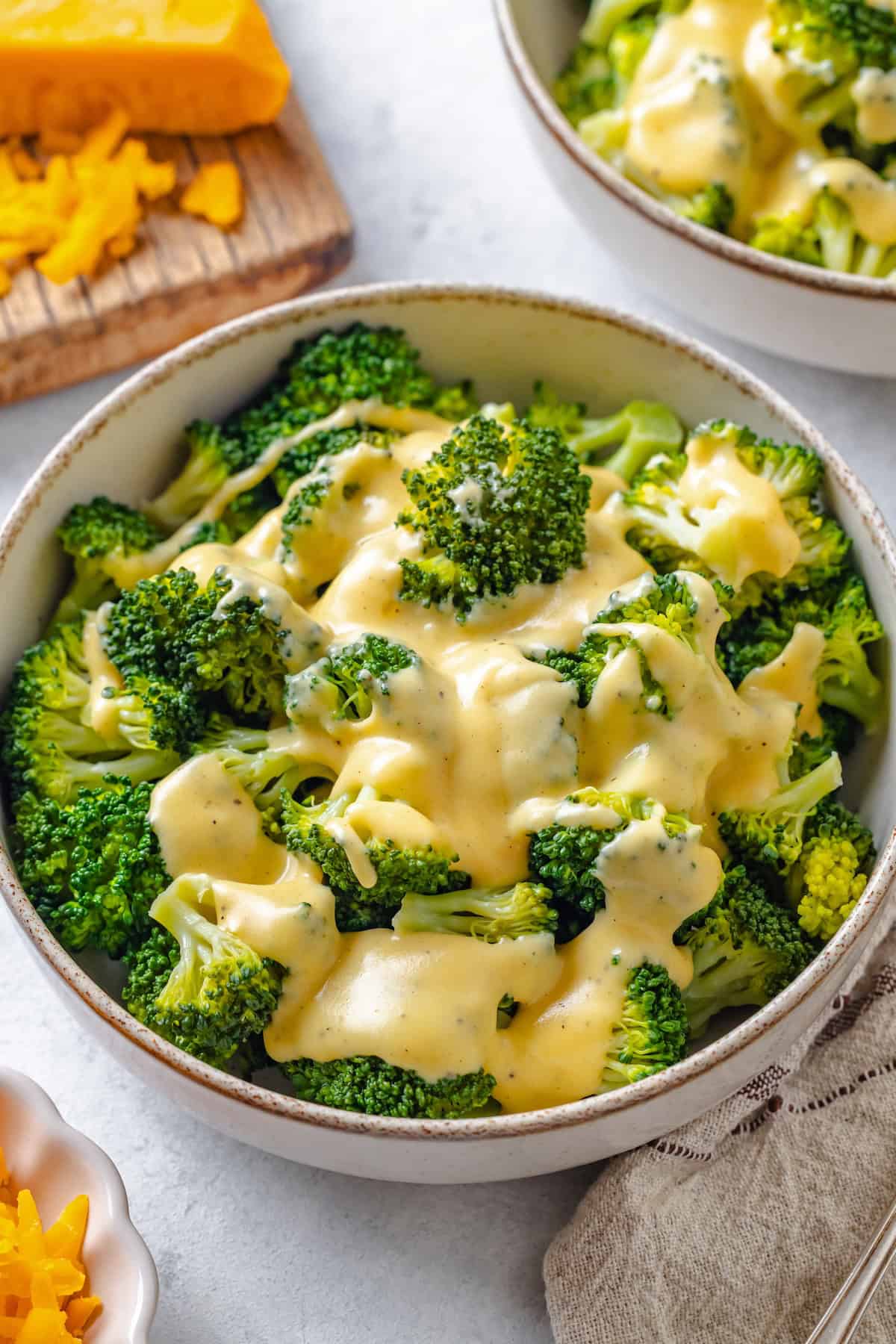 Close up of a bowl of steamed broccoli topped with a creamy cheddar sauce.