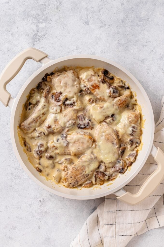 Melted mozzarella cheese over a chicken and mushroom mixture in a white skillet.