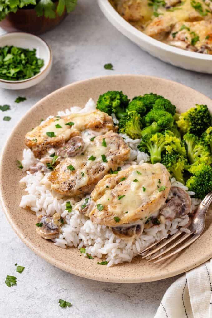 Sliced chicken with mozzarella and a cream cheese sauce served over rice alongside some steamed broccoli on a dinner plate.