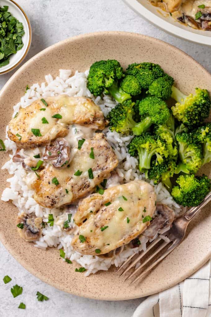 Cream cheese chicken served over white rice with a side of steamed broccoli on a dinner plate.