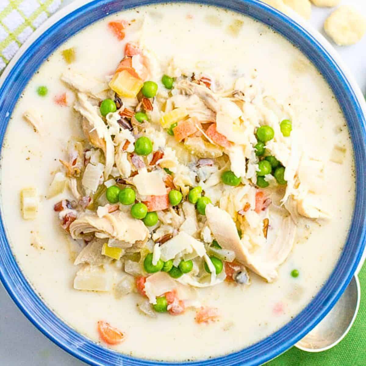 Close up of a creamy chicken and rice soup with peas and carrots in a blue bowl.
