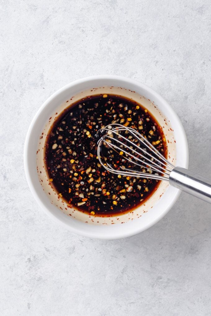 A whisk resting in a small bowl with a soy sauce and garlic sauce mixture.
