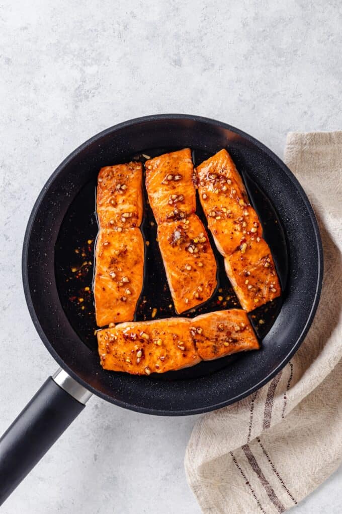 Salmon filets topped with a soy sauce and garlic sauce in a dark skillet.