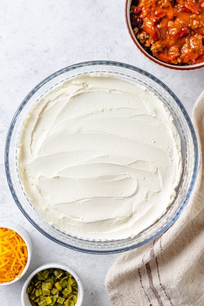 A glass pie plate with cream cheese spread in an even bottom layer.