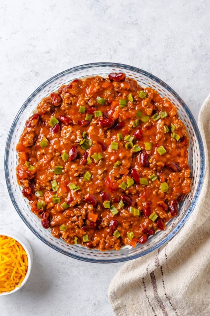 Diced green chiles spread out over canned chili in a glass pie plate.