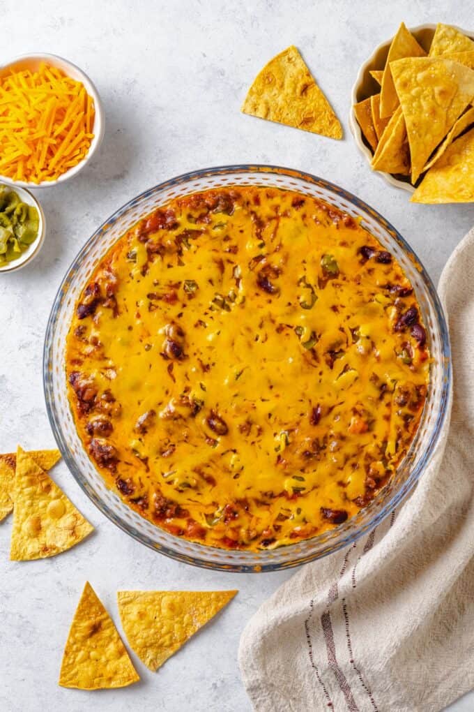 Cheesy baked Mexican dip in a glass pie plate with chips scattered around.