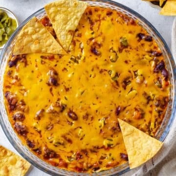 Close up of chips resting on the sides of a glass pie plate with a cheesy baked Mexican dip with canned chili.