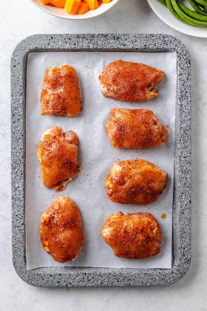Seasoned chicken thighs on a parchment paper lined baking sheet before being cooked.