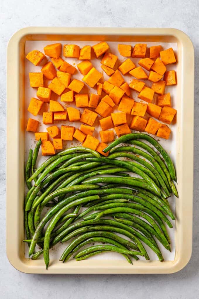 Cubed sweet potatoes and green beans arranged on a parchment paper lined baking sheet before being cooked.