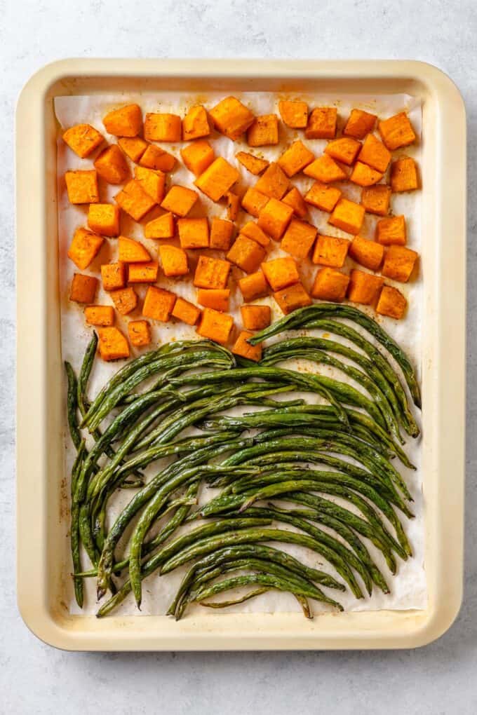 Roasted sweet potatoes and green beans on a parchment paper lined baking sheet.