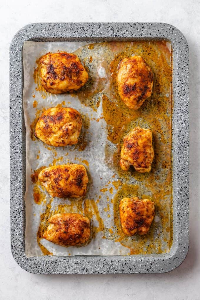 Baked seasoned chicken thighs on a parchment paper lined baking sheet.