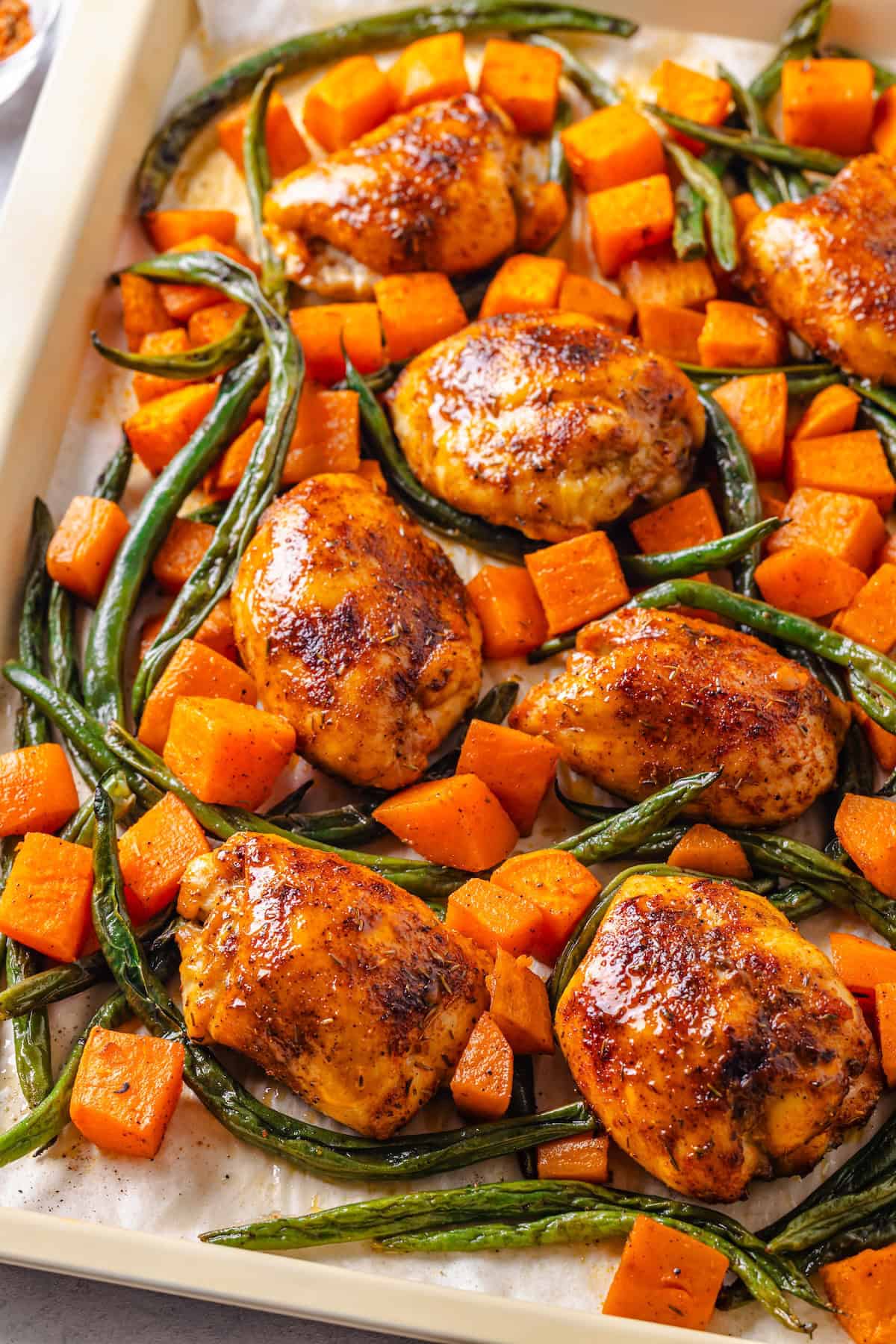 A sheet pan dinner with chicken thighs, sweet potatoes and green beans.