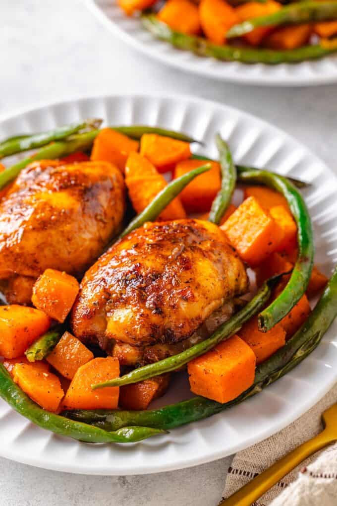A white dinner plate with roasted chicken thighs, sweet potatoes and green beans.