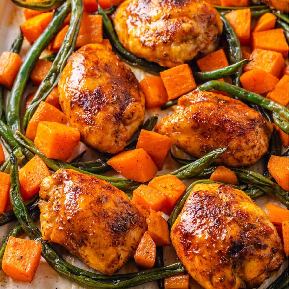 Close up of a sheet pan dinner with chicken thighs, sweet potatoes and green beans.