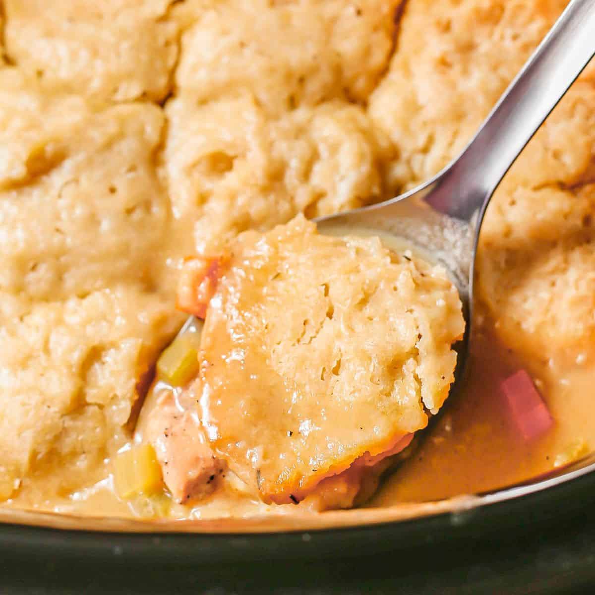 A serving spoon lifting some chicken and dumplings from a slow cooker insret.