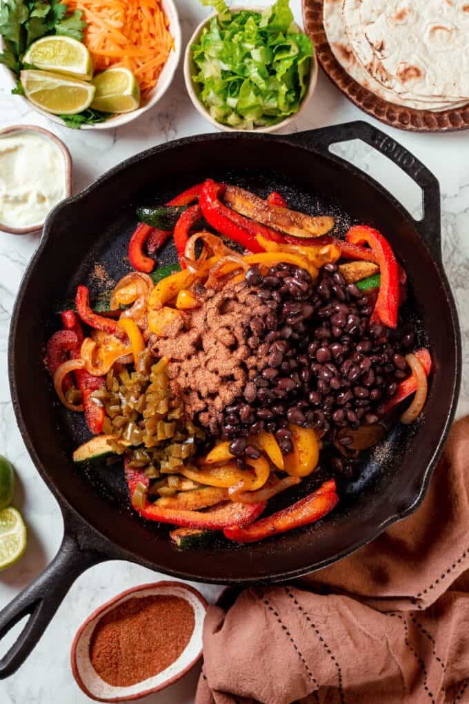 Sautéed onions, bell peppers and zucchini with black beans, green chilies and fajita seasoning piled on top in a cast iron skillet.