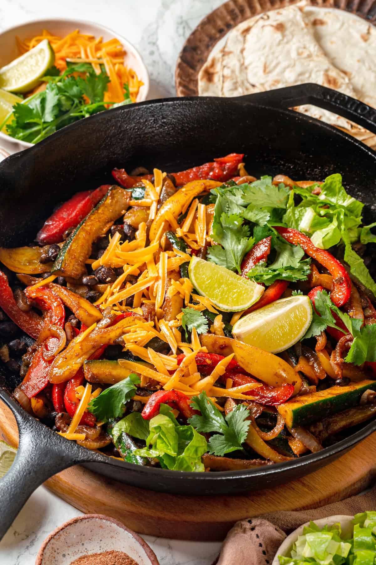 A black bean and veggie fajita skillet with cheese, cilantro and lime wedges on top.
